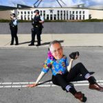 An Extinction Rebellion activist wears a mask depicting Australian Prime Minister Scott Morrison blocks the road during a protest outside Parliament House in Canberra. (AAP Image/Lukas Coch)